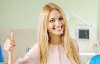Smiling Young Woman at Dentist Office Showing Her Thumb Up