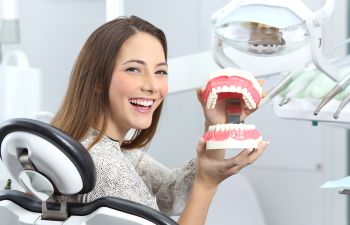 Cheerful Girl in Dental Chair Holding Dental Model