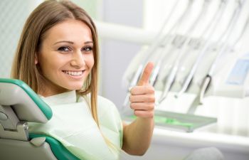 relaxed smiling woman in a dental chair showing her thumb up