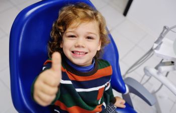 A little boy in a dental chair showing his thumb up.
