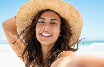 cheerful girl on the beach holds a hat on head